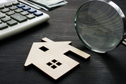 Property assessment. Wooden house with magnifier and calculator.